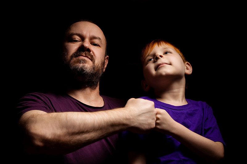 在黑色背景下,父子俩面带微笑,互挥拳头亲子互动父亲节的概念