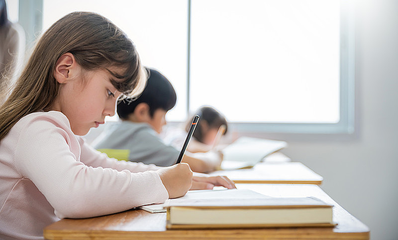 在小学的教室里,白人小学生在课桌上写字.女学生在小学做测试.