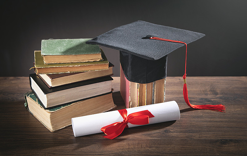 毕业帽、书和毕业证放在木桌上。