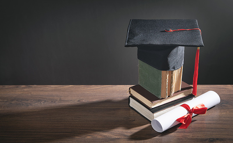 毕业帽、书和毕业证放在木桌上。