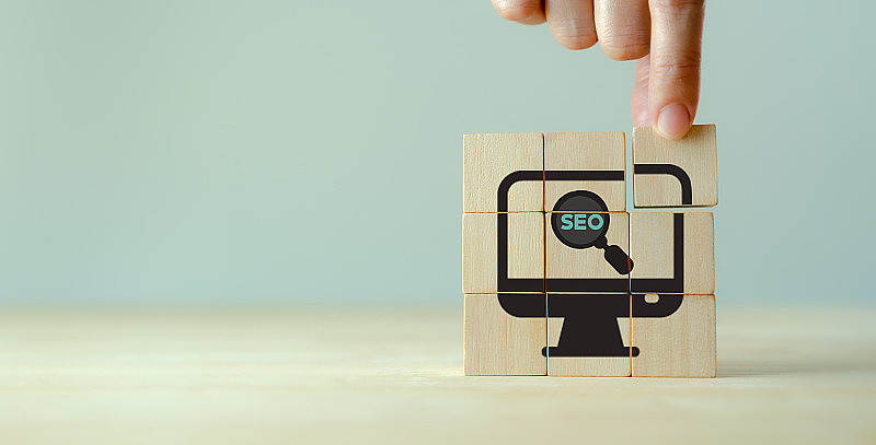 SEO，搜索引擎优化排名的概念。促进网站流量的数字化营销策略。手握木制立方体与图标的放大镜与字母缩写SEO。