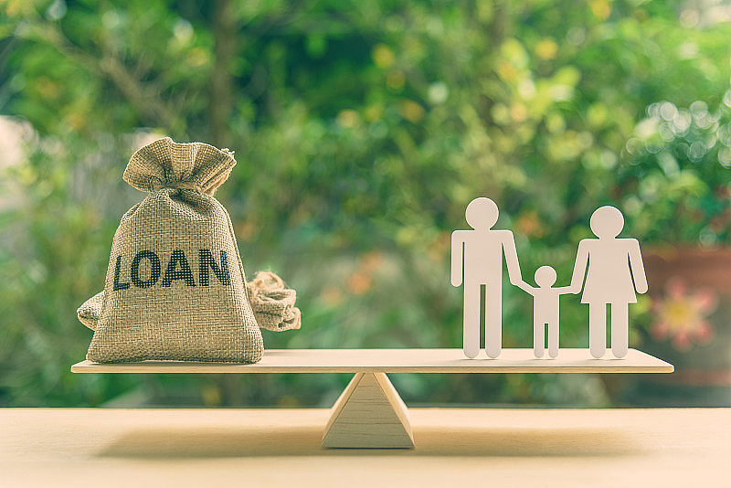 家庭金融/金融贷款和风险管理概念:贷款袋，白色亚克力切割(爸爸，妈妈，儿子)在基本的平衡天平。