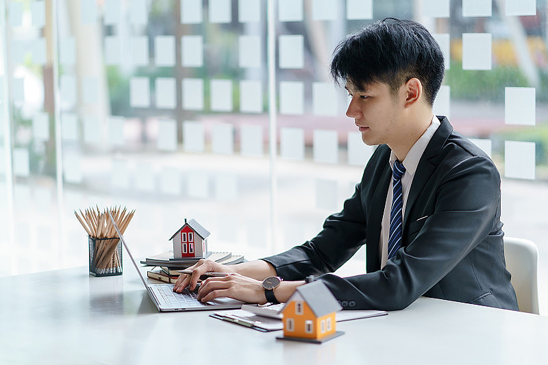 亚洲男性房地产经纪人使用笔记本电脑。对房屋买卖合同的批准提供按揭贷款和家庭保险的概念。