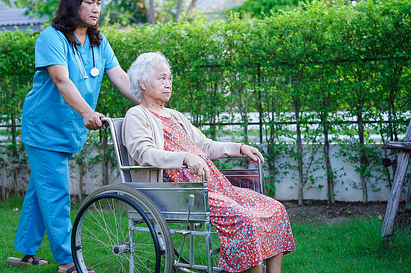 医生帮助亚洲老年残疾妇女坐在公园轮椅上，医学概念。
