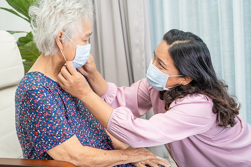 护工在公园帮助和交谈亚洲老人或老年妇女，戴着口罩保护安全感染covid - 19冠状病毒。