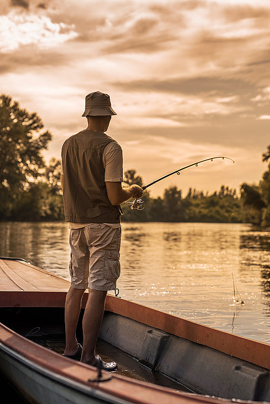 一个渔民在日落时从船上捕鱼的后视图。