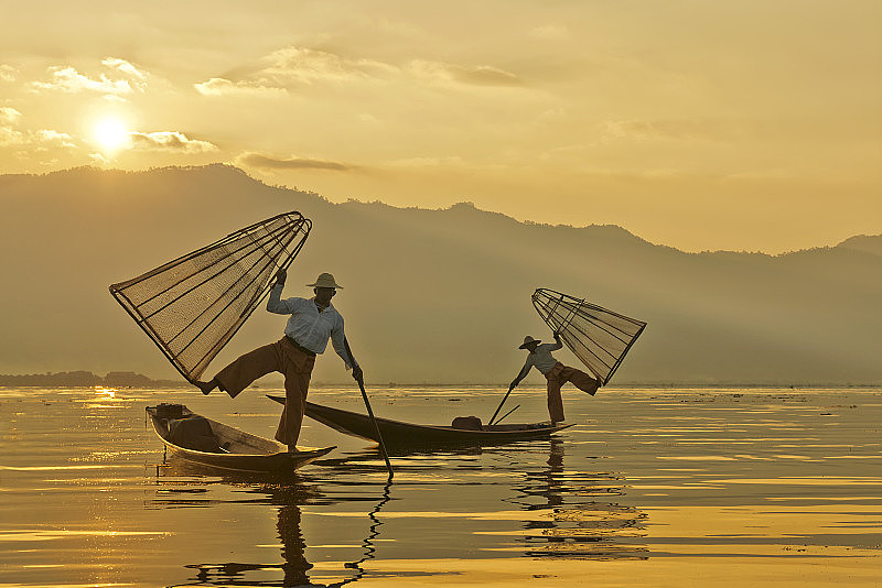 在日出的茵莱湖上用传统捕鱼器的渔民