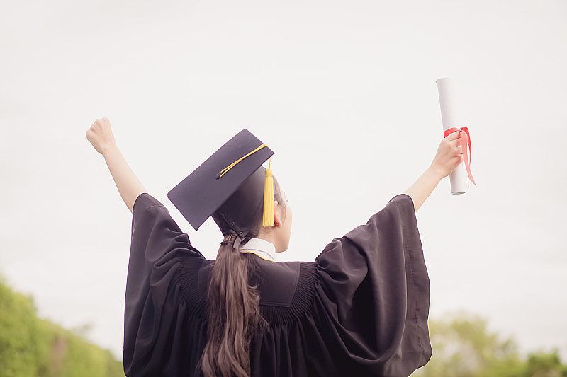 毕业生举起手来，手拿证书庆祝，为教育的成功感到幸福
