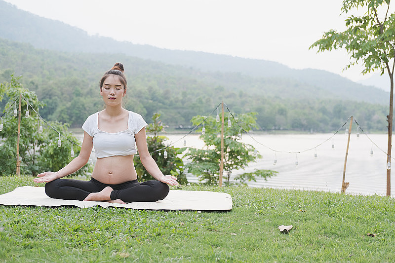 一名亚洲孕妇坐在公园的草地上练习瑜伽。在产科冥想。健康的生活方式和放松的理念。