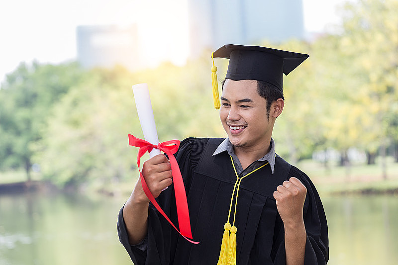 毕业的亚洲人戴着学士帽和学士服，手拿证书庆祝