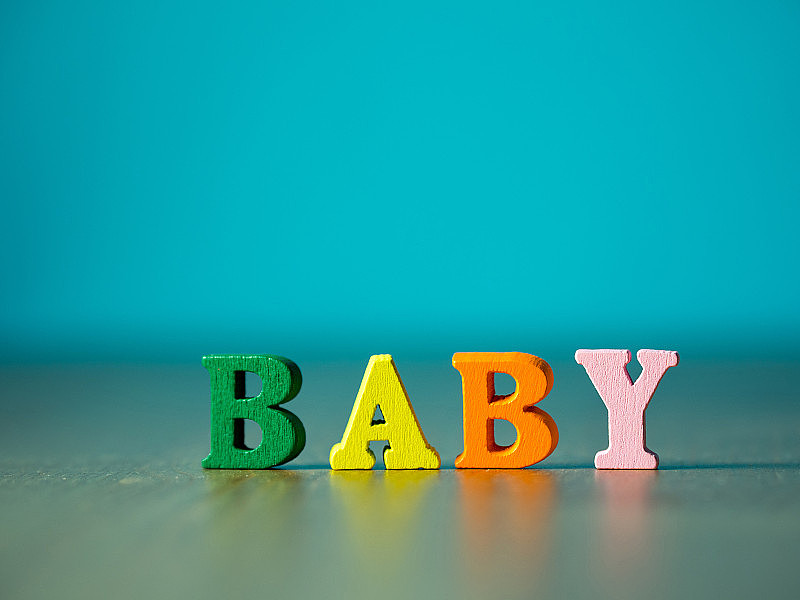 婴儿。英文字母颜色由木制字母构成。木桌上的字母宝宝，背景是粉蓝色。