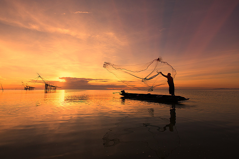 亚洲渔民在木船上撒网，在日出前的清晨在自然河流中捕鱼