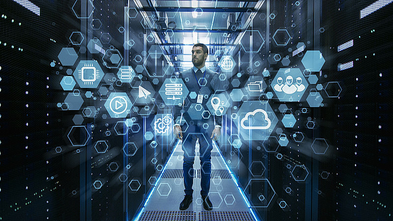 Curios IT工程师站在工作中的数据中心服务器机房中间。云和互联网图标可视化前景。