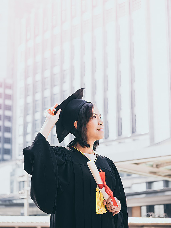毕业那天，亚洲女人拿着毕业帽和毕业礼服，拿着文凭，成功的理念